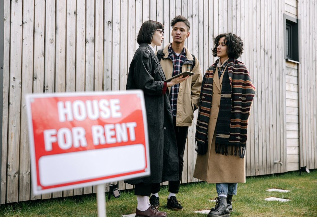 realtor talking to couple beside house for rent sign
